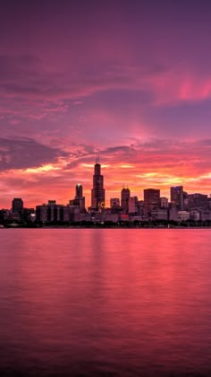 the city skyline is lit up at night with pink and purple clouds in the sky