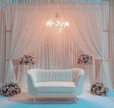 a white couch sitting under a chandelier in front of a curtained wall