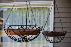 two hanging baskets on the side of a house, one with a heart shaped decoration