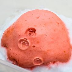 a pink substance in a plastic container on top of some white paper with water droplets