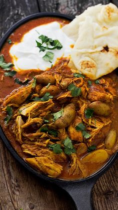 a skillet filled with meat and potatoes on top of a wooden table next to pita bread