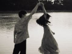 two people jumping in the air near water with trees in the background and one person holding his arms up