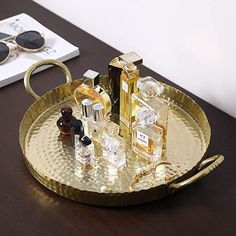 a gold tray with perfume bottles and sunglasses on it next to a pair of glasses