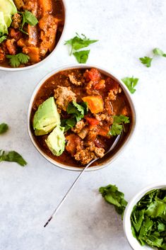 two bowls filled with chili, meat and avocado garnished with cilantro