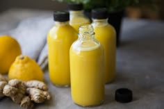 three bottles filled with yellow liquid next to lemons and ginger