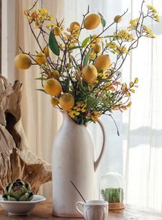 a white vase filled with yellow flowers on top of a wooden table next to a cup