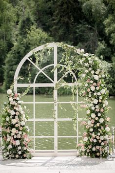 an arch decorated with flowers and greenery stands in front of the water at a wedding ceremony