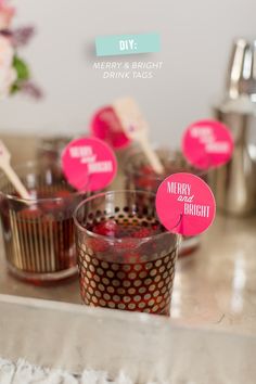 cupcakes with pink paper tags on them sitting on a counter next to cups