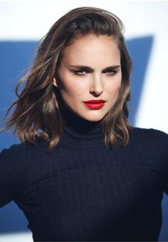 a woman with long hair wearing a black turtle neck sweater and red lipstick, standing in front of a blue wall