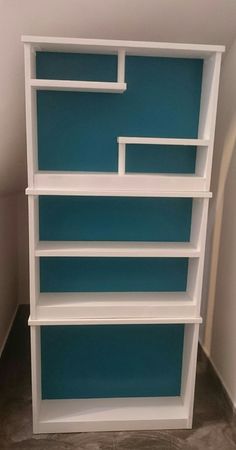 a white book shelf with blue shelves on the top and bottom, against a wall