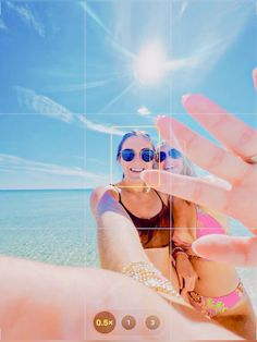 two women in bikinis are holding up their hands to take a photo on the beach