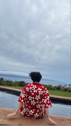 a woman sitting on the edge of a pool looking out at the water and clouds