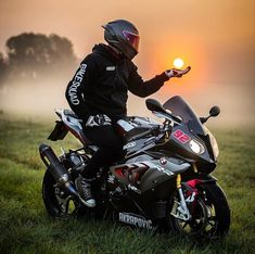 a person sitting on a motorcycle with the sun setting behind them and fog in the air