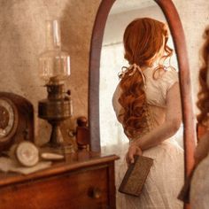 a woman with red hair is looking at herself in the mirror and holding a book