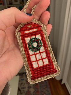 a hand holding a needled ornament in the shape of a phone booth