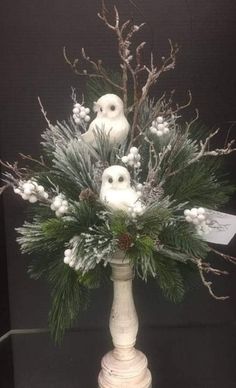 a white vase filled with lots of snow covered plants and birds sitting on top of it