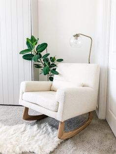 a white rocking chair next to a potted plant in the corner of a room