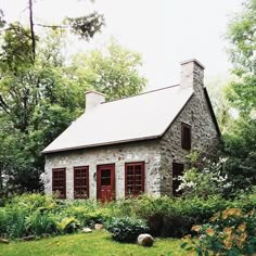 a small stone cottage with red doors and windows sits in the middle of a lush green yard