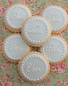 four decorated cookies with names on them sitting on a floral tablecloth covered table cloth