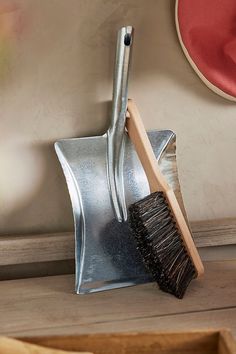 a metal dustpan and brush sitting on top of a wooden floor next to a wall