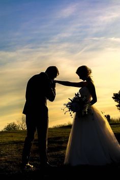 a bride and groom standing in the grass at sunset