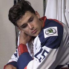 a young man sitting in front of a window with his hand on his chin and looking at the camera