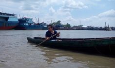 a person in a small boat on the water with two boats behind them and one is holding a stick