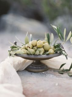 some olives are sitting on a plate with white cloth around it and green leaves