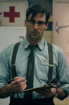 a man with glasses and suspenders holding a clipboard