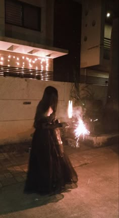 a woman in a long black dress holding sparklers