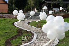 some white balloons are floating in the air on top of a stone path that is surrounded by grass