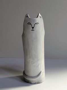 a white ceramic cat figurine sitting on top of a table next to a wall