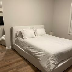 a large white bed sitting in a bedroom next to a window with blinds on the windowsill