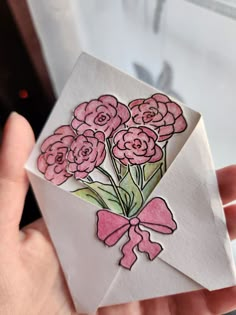 a hand holding an envelope with pink flowers in the center and a bow on it