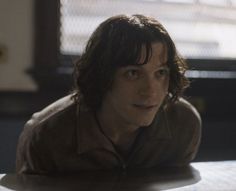 a young man sitting at a table with his head turned to the side and looking off into the distance