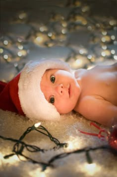 a baby wearing a santa hat laying on top of a bed covered in christmas lights