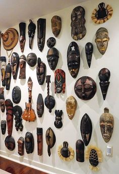 a wall full of masks on display in a room with wood floors and white walls