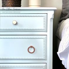 a close up of a white dresser on a bed with a lamp in the background