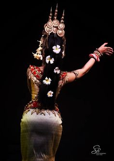 a woman with black hair and white flowers on her head is dressed in an elaborate costume