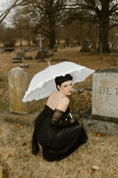 a woman sitting on the ground with an umbrella over her head in front of a grave