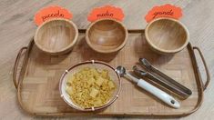 a tray with bowls and spoons on it that have food in them, along with utensils