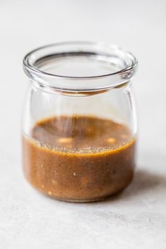 a glass jar filled with brown liquid sitting on top of a white countertop next to a wooden spoon