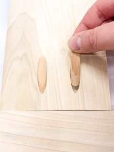 a hand is holding a piece of wood near the edge of a piece of plywood