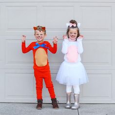 two children dressed in costumes standing next to each other with their hands up and smiling