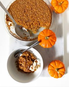 a bowl of oatmeal and two small pumpkins on a white table