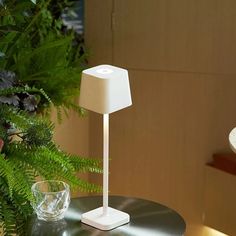 a white lamp sitting on top of a table next to a glass cup and plant