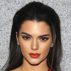 a woman with long black hair wearing red lipstick and diamond earrings on her head, looking at the camera