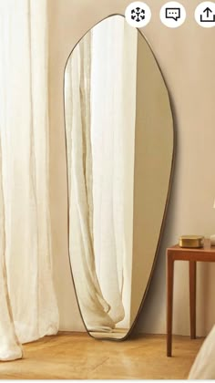 a large oval mirror sitting on top of a wooden floor next to a lamp and table