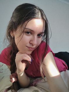 a young woman laying on top of a bed next to a white wall and looking at the camera