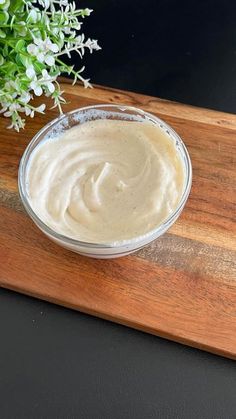 a bowl of white sauce sitting on top of a wooden cutting board next to a plant